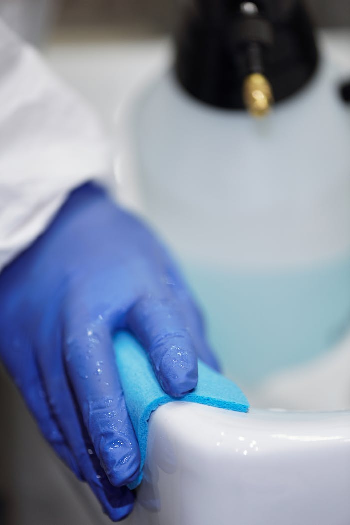 services-03 A blue-gloved hand using a sponge to clean a white sink in a hygienic environment.
