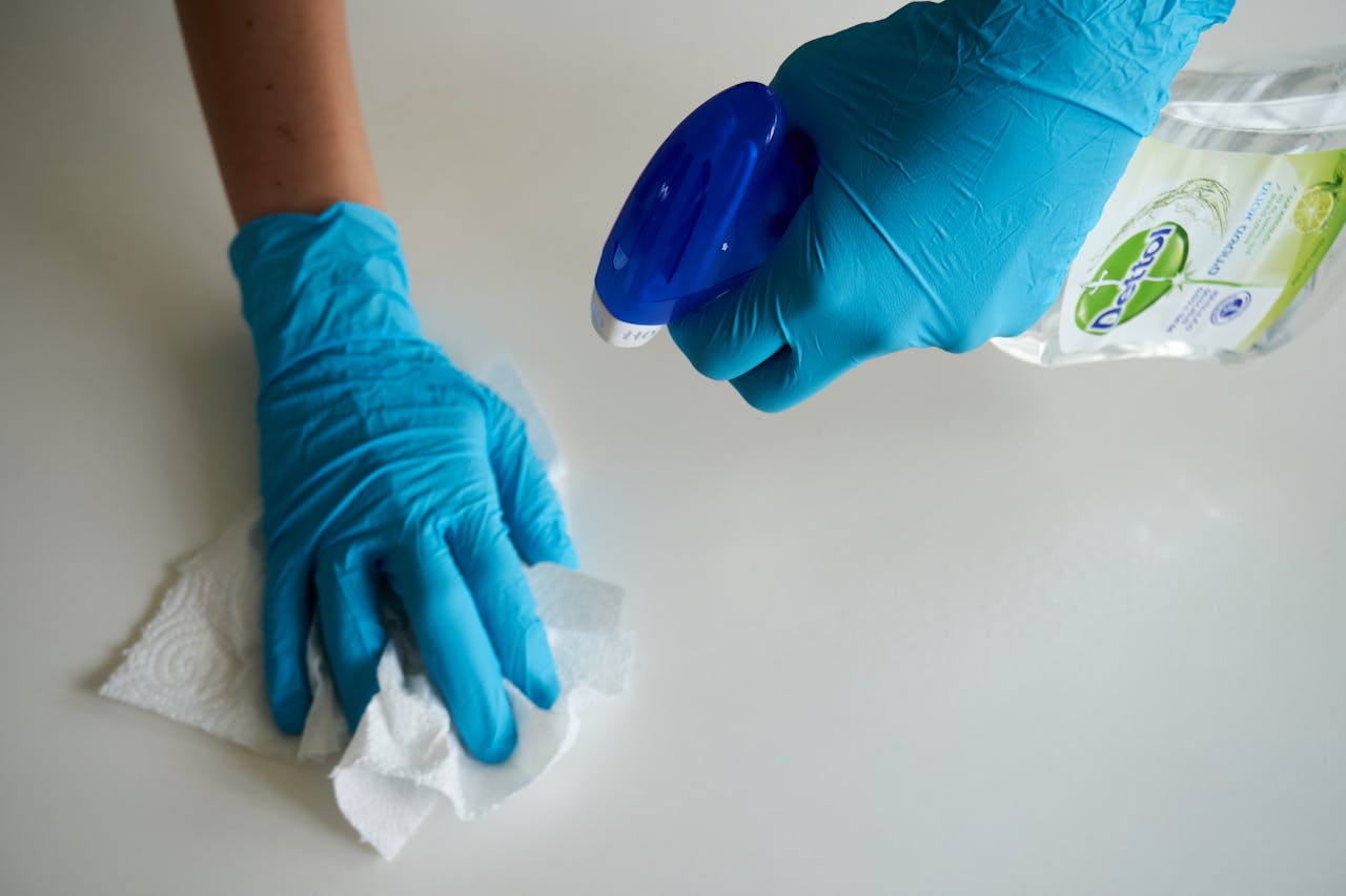 services-04 Close-up of hands wearing gloves cleaning a surface with disinfectant spray.