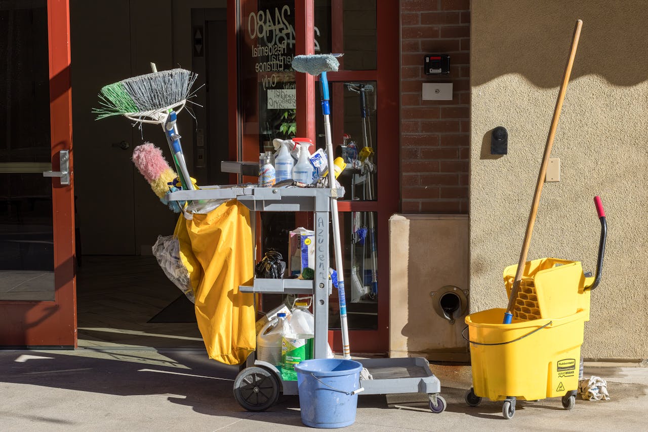 about-01 Cleaning supplies and tools outside a building entrance bathed in sunlight.